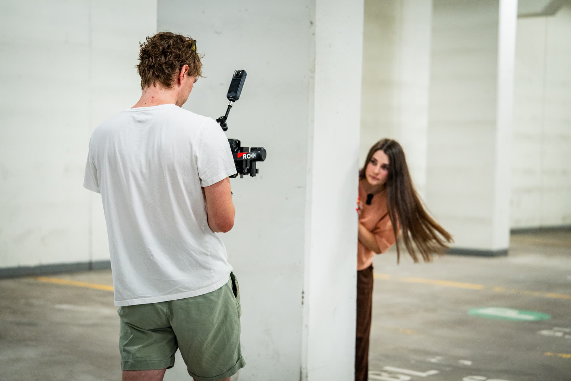 A model peeking out from behind a pillar while a videographer films